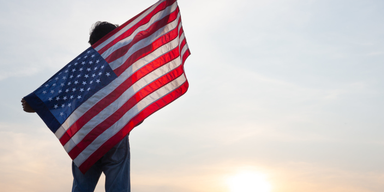 man standing and holding USA flag ิat sunrise view